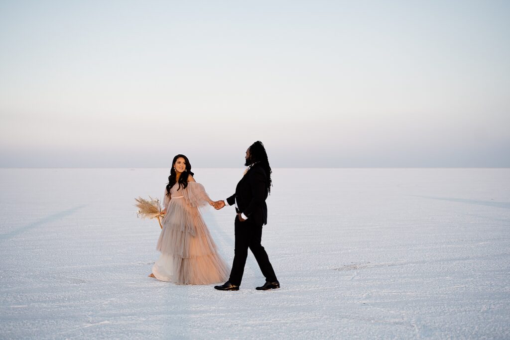 Utah elopement photographer captures couple walking through Salt Flats elopement wearing Salt Gowns dress