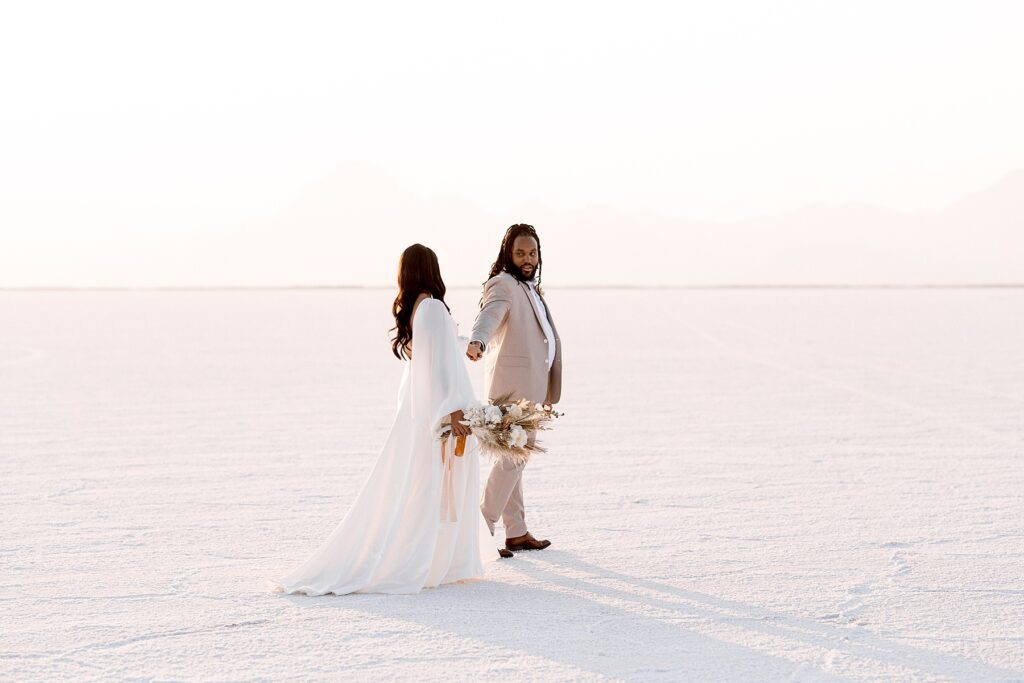Utah elopement photographer captures groom holding bride's hand before Salt Flats wedding