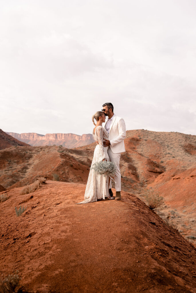 bride and groom standing together embracing on top of red rock arch