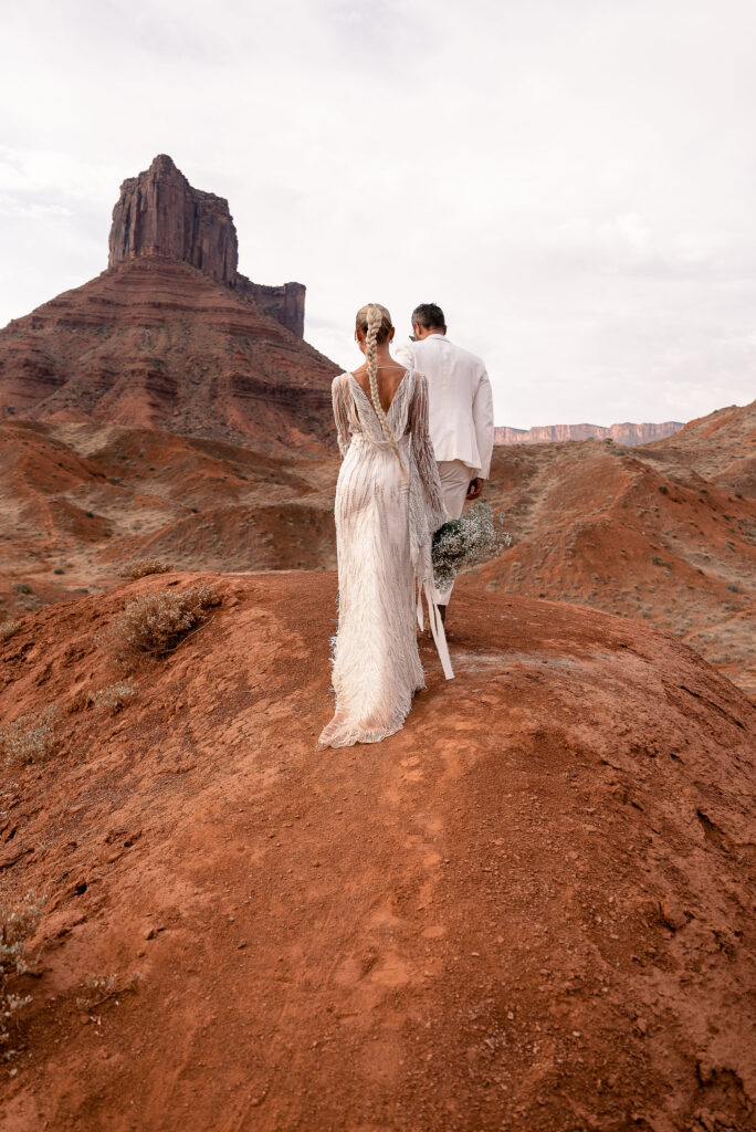 bride and groom walking together on red rock arch