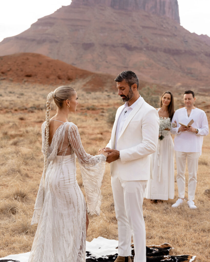 Moab elopement photographer captures groom holding bride's hand while reading vows