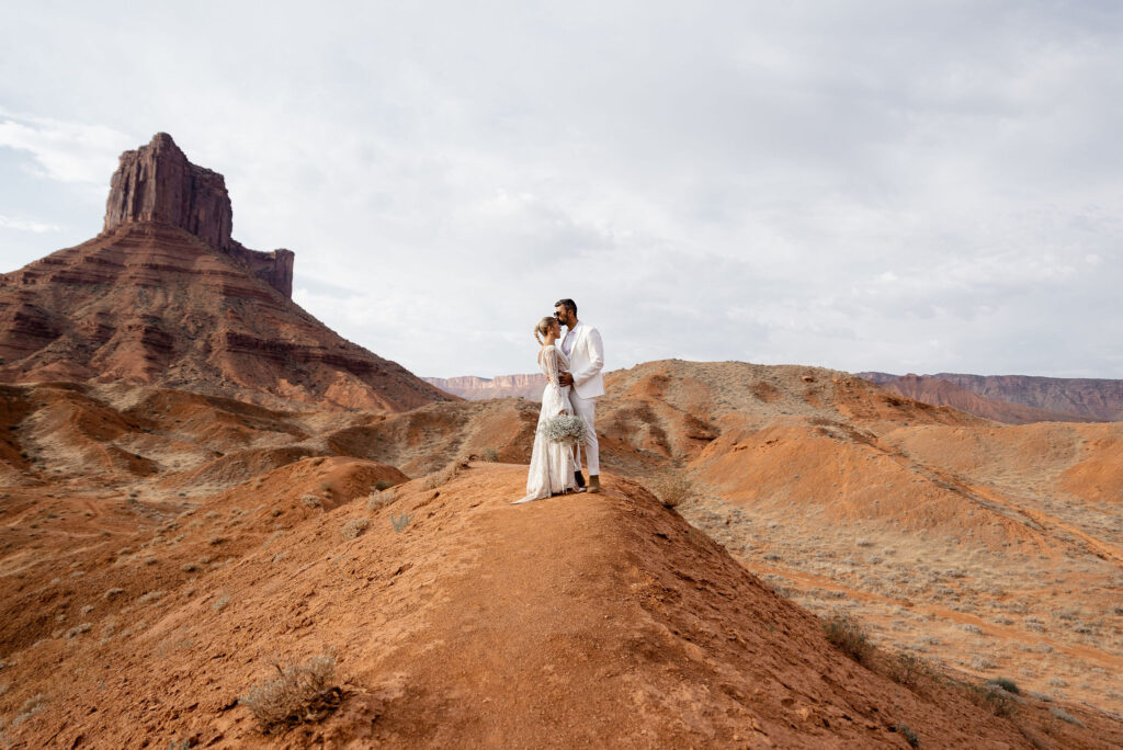 Moab elopement photographer captures bride and groom standing together on Moab red rock after sunrise elopement