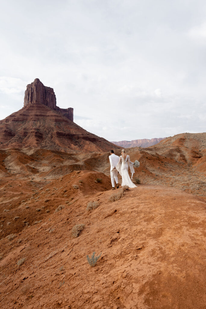 Moab elopement photographer captures couple walking hand in hand on red rock arches