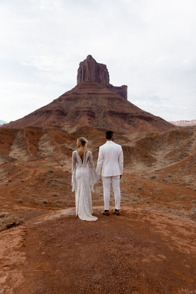 bride and groom holding hands looking over red rock in moab