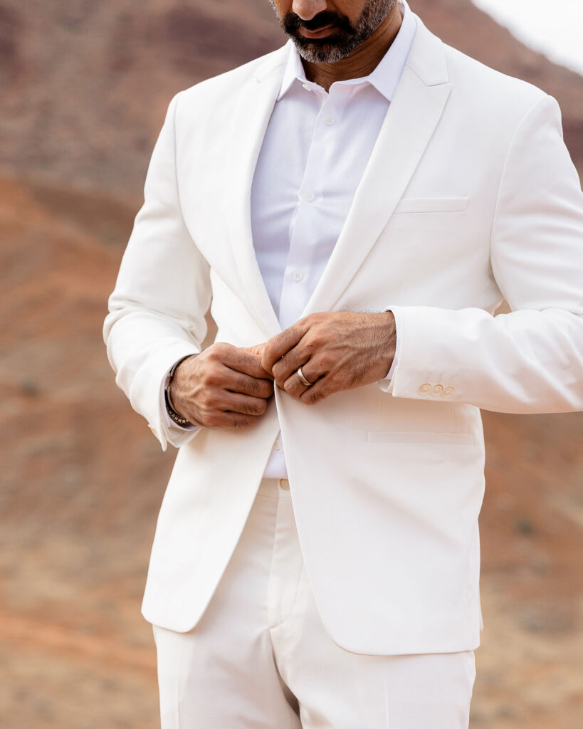 close up of groom buttoning white suit jacket 