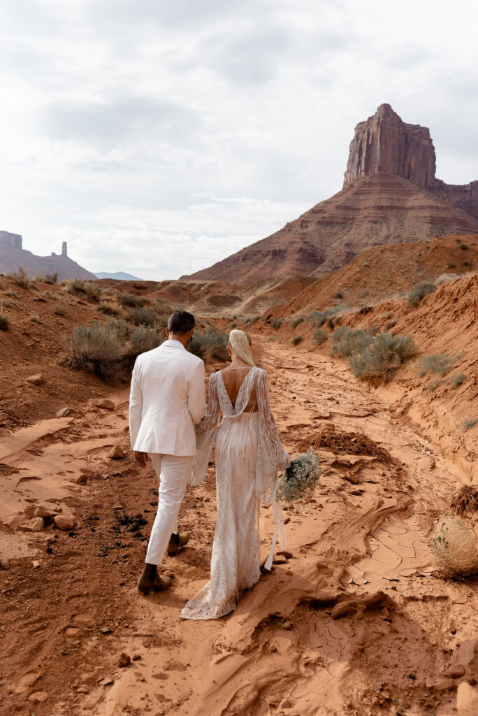 bride and groom walking towards tall arch in Moab