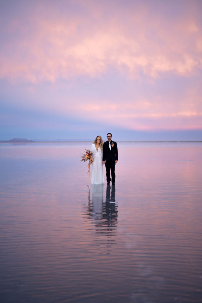 Utah elopement photographer captures couple walking through flooded salt flats during blue hour