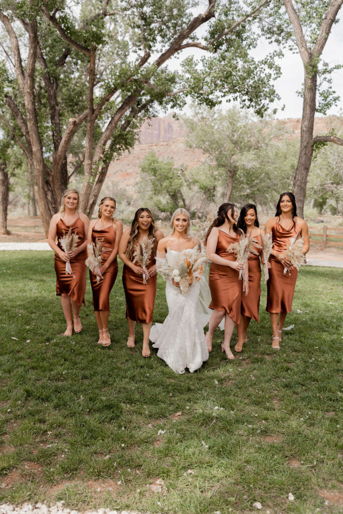 Utah elopement photographer captures bride walking with bridesmaids in terracotta colored gowns