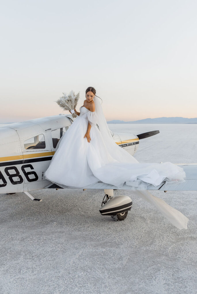Utah elopement photographer captures bride standing on airplane wing at luxurious salt flats wedding