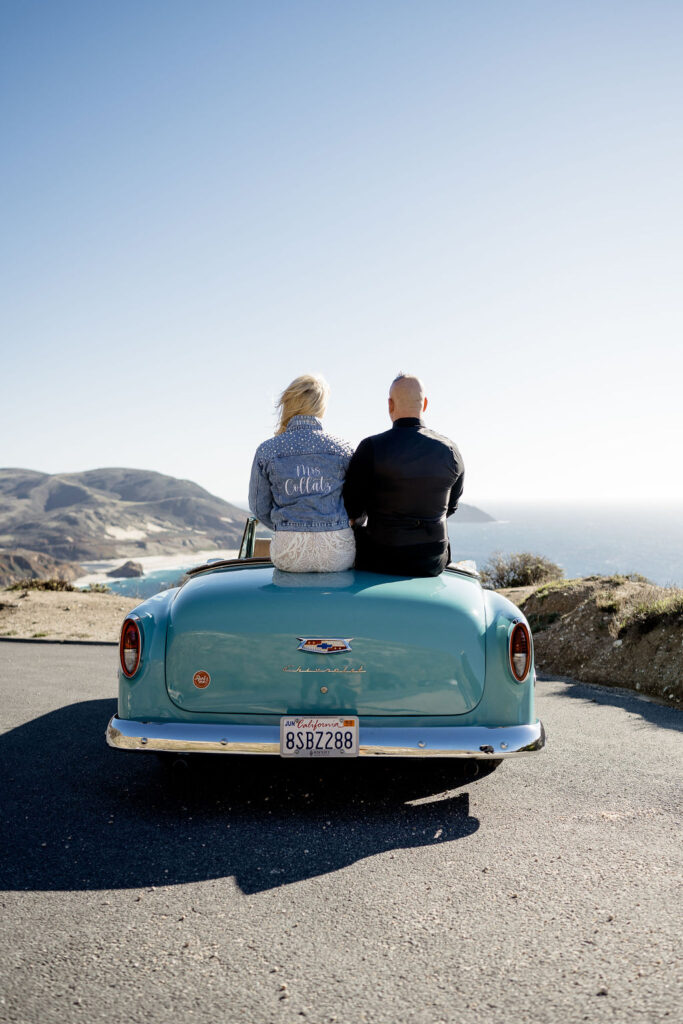 Big Sur elopement photographer captures couple sitting on car wearing wedding attire