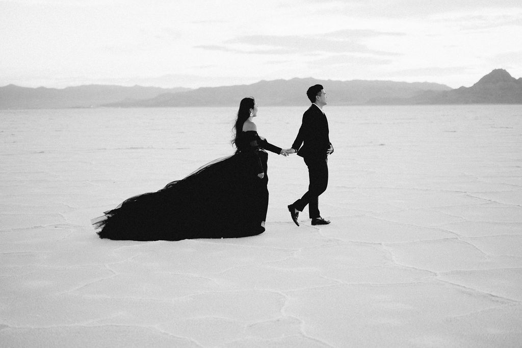 Utah elopement photographer captures couple walking along salt flats in black outfits