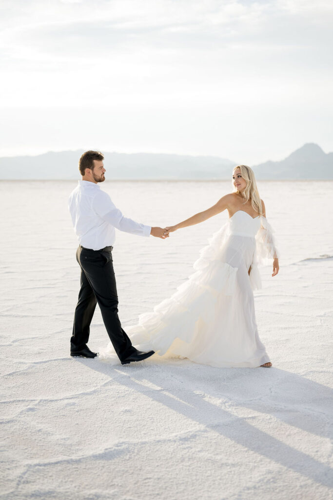 Utah elopement photographer captures woman holding man's hand during salt flats engagements