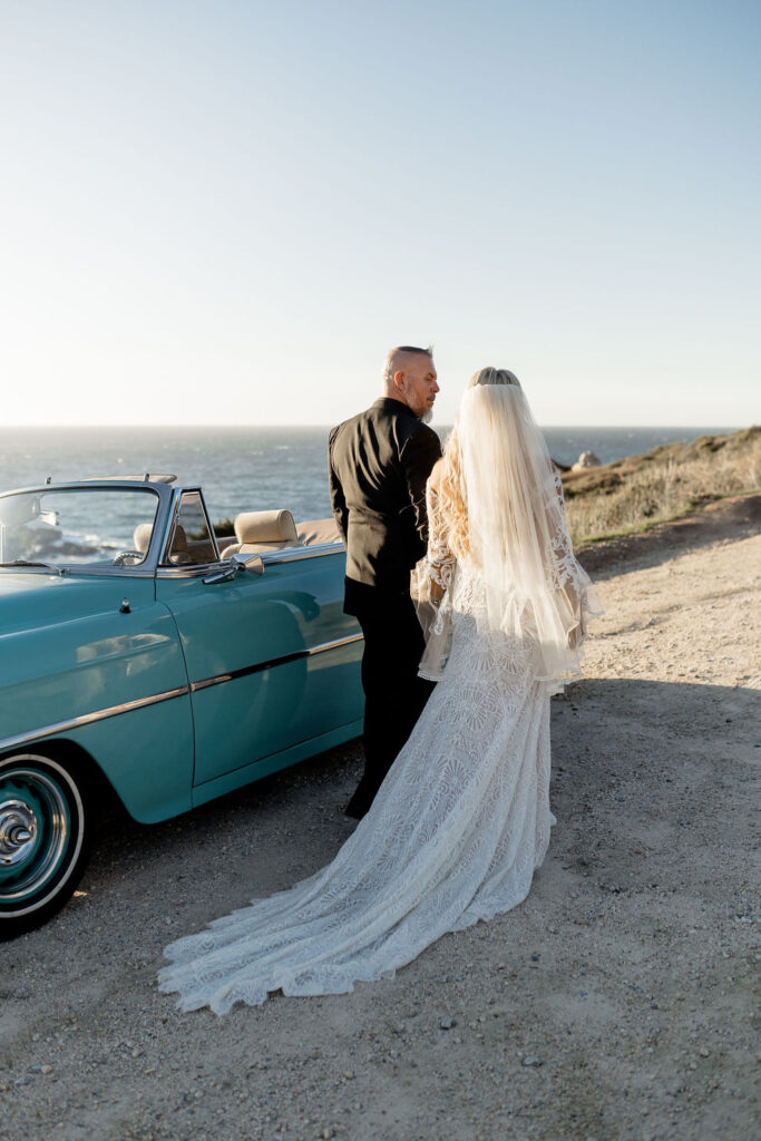 Big Sur elopement photographer captures couple walking alongside blue vintage car