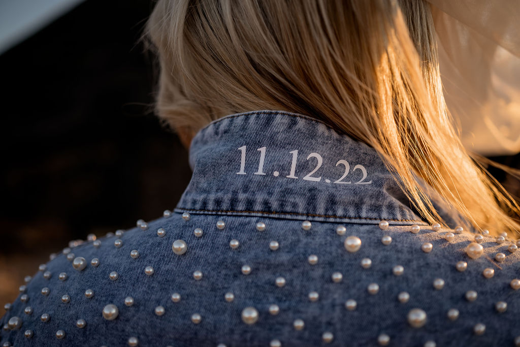 Big Sur elopement photographers captures back of bridal jean jacket with pearls and wedding date