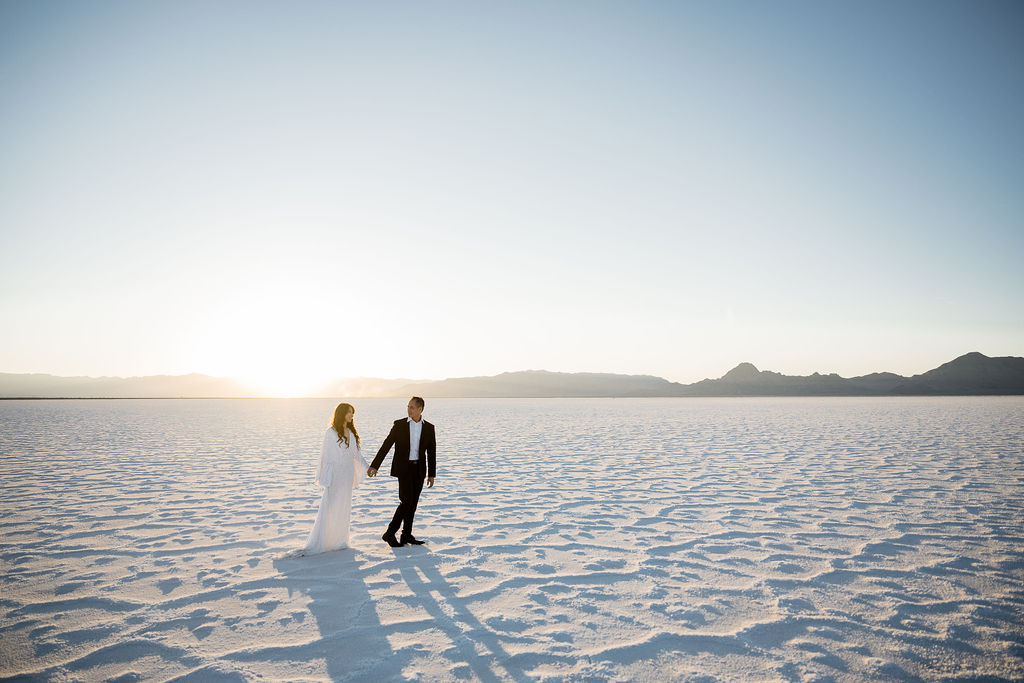 couple walking across the salt flats at sunset in white dress and black suit