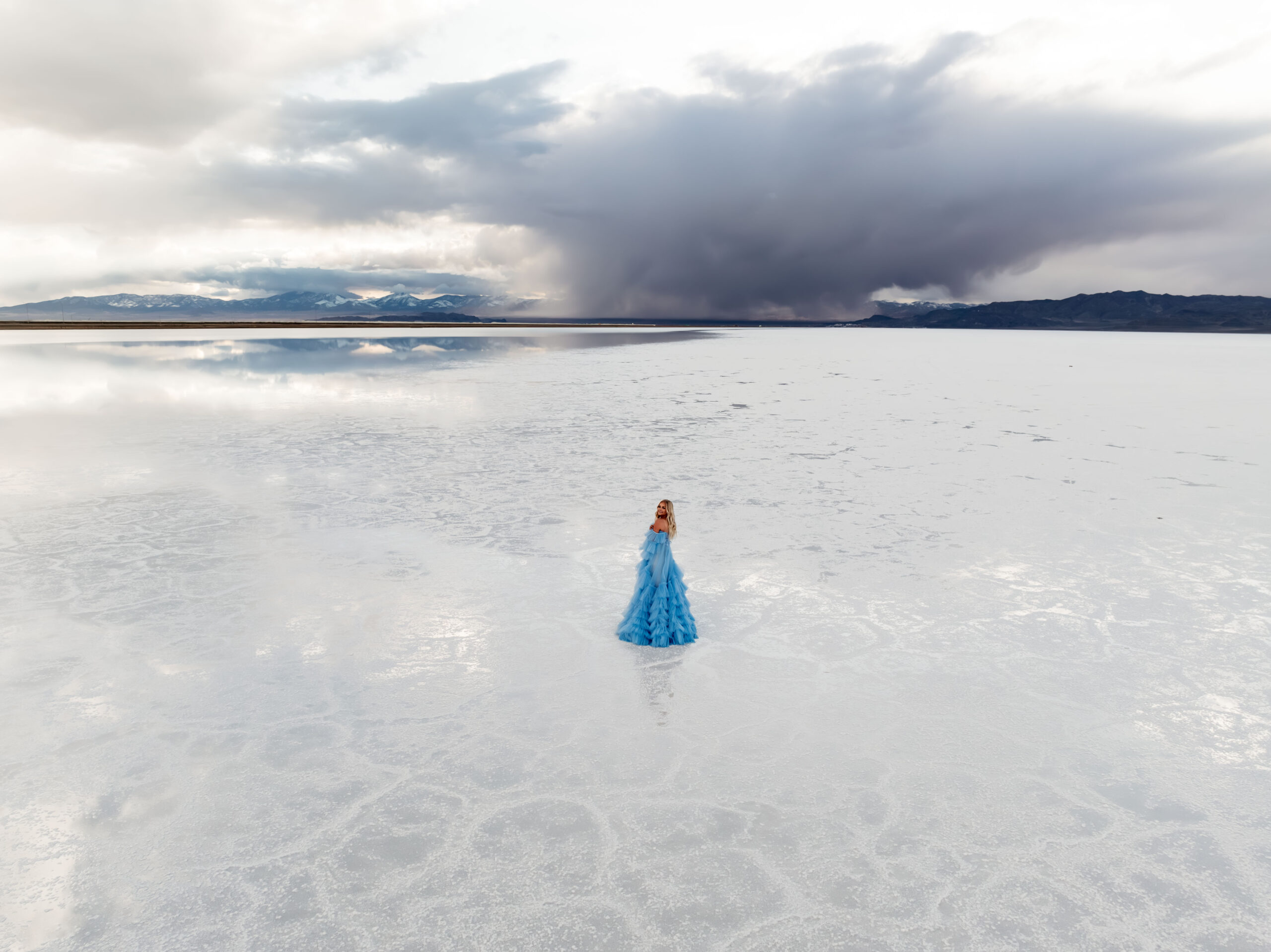 Dreamy landscape of the Utah Salt Flats featuring a woman in a fairy-tale blue dress, blending with the horizon.