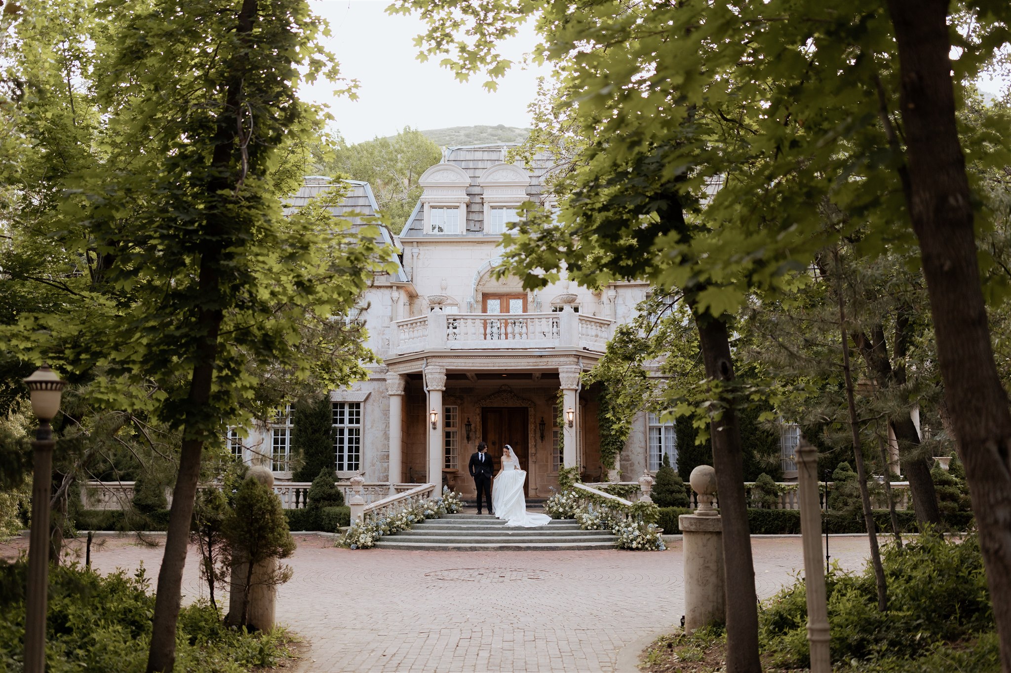 Bride and groom standing in front of La Caille Château surrounded by trees, luxury Utah wedding venue