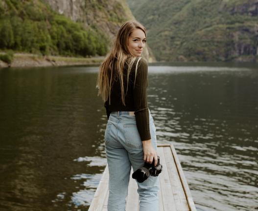 Dani Purington, a top photographer in Utah, smiles with her camera in front of a lake.