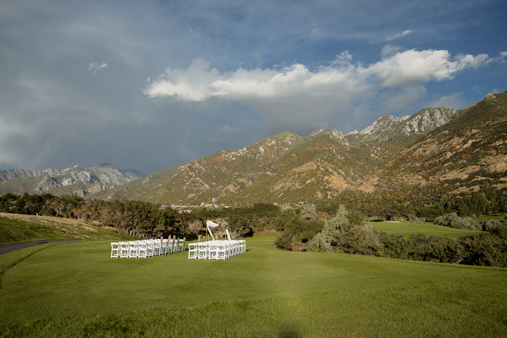 Outdoor Utah wedding venue with panoramic mountain views, ceremony setup featuring white chairs and floral arrangements under a clear blue sky.