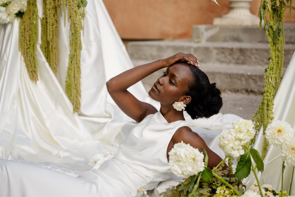 Bride lounges on the steps of her Utah wedding venue in her long white dress.