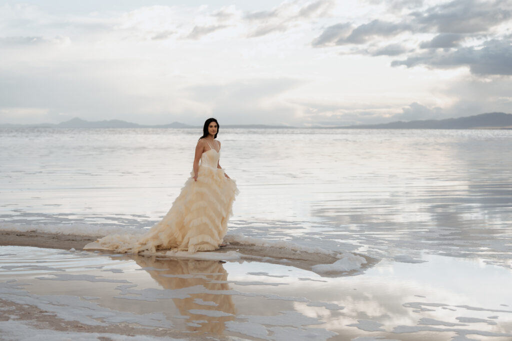 Bride wearing a wedding dress standing beside Pink Lake, with the colorful water reflecting the scene.