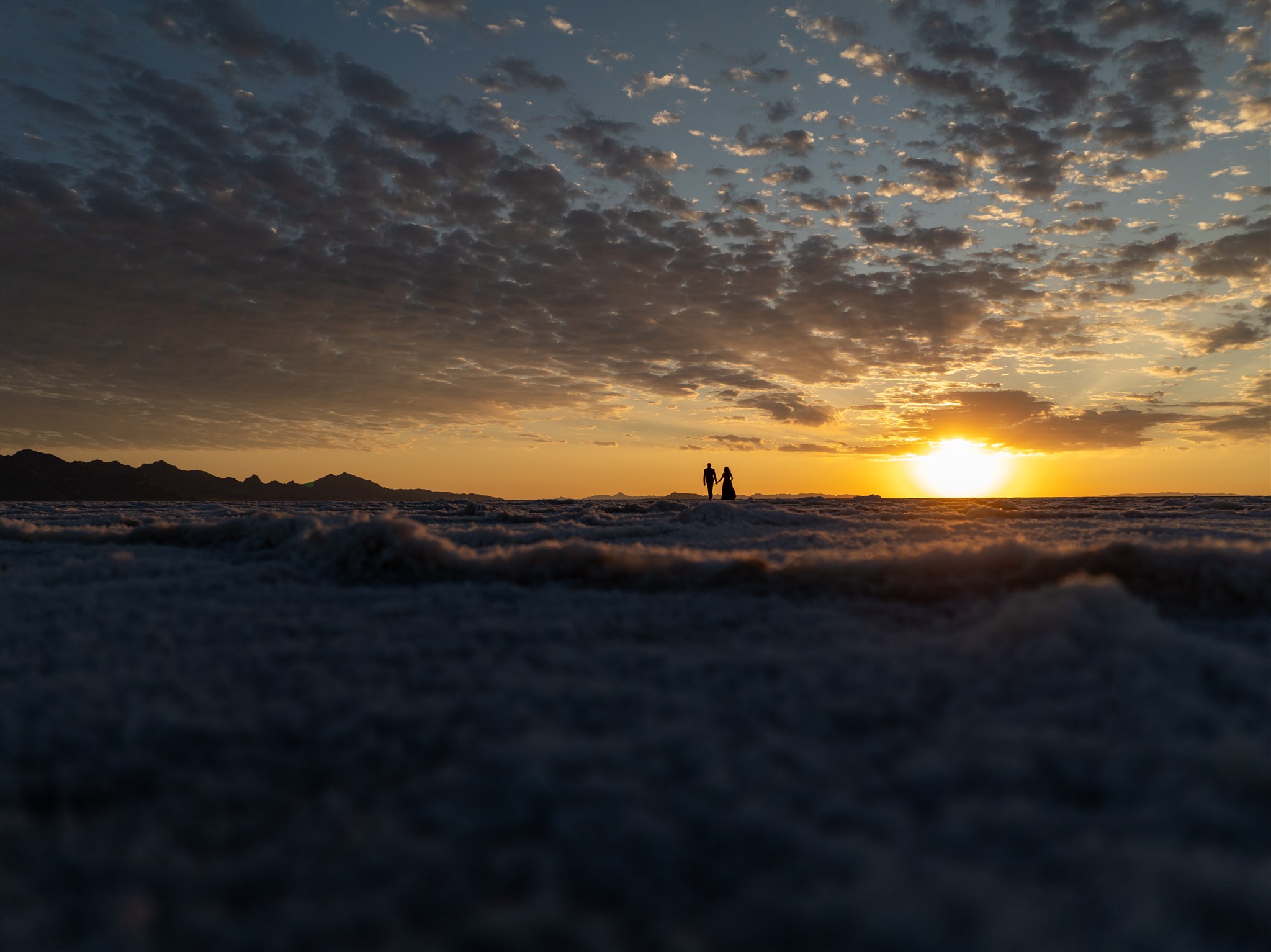 Couple who just got married in Salt Flats holding hands underneath the setting sun on their wedding day.