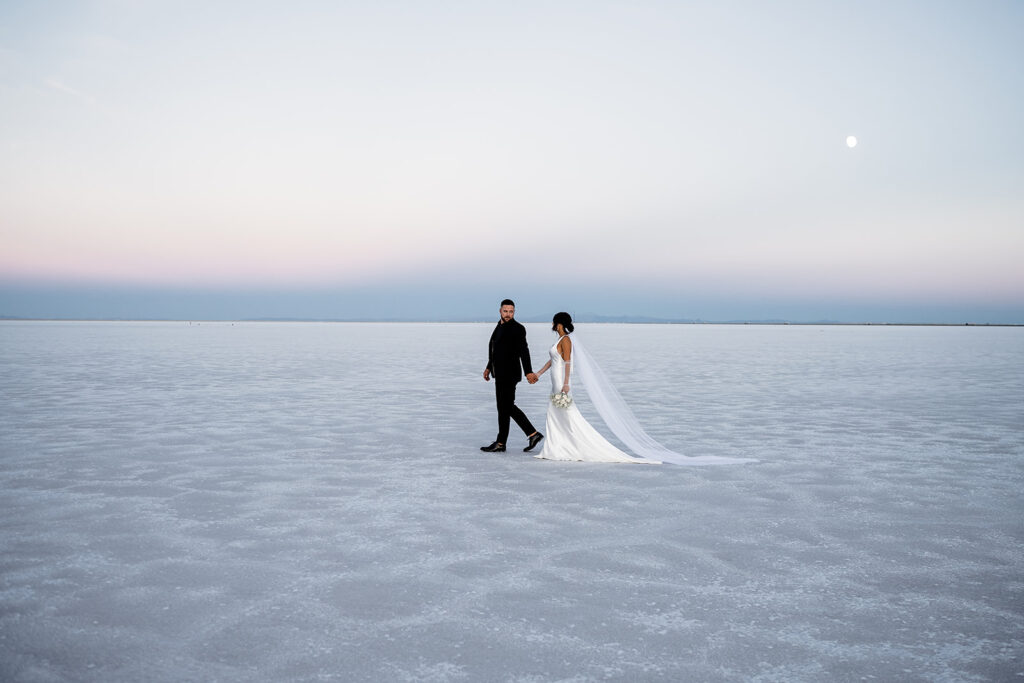 Wide-angle shot of a couple standing in the vast open space of the Salt Flats at sunset.