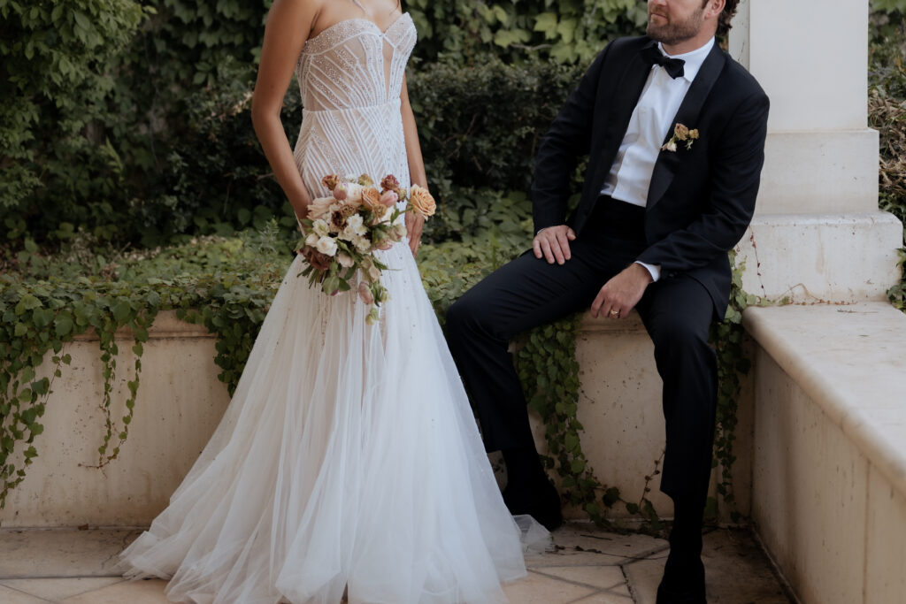 Close-up of a bride and groom, with the photo focusing on their wedding outfits and details while their faces are out of frame.