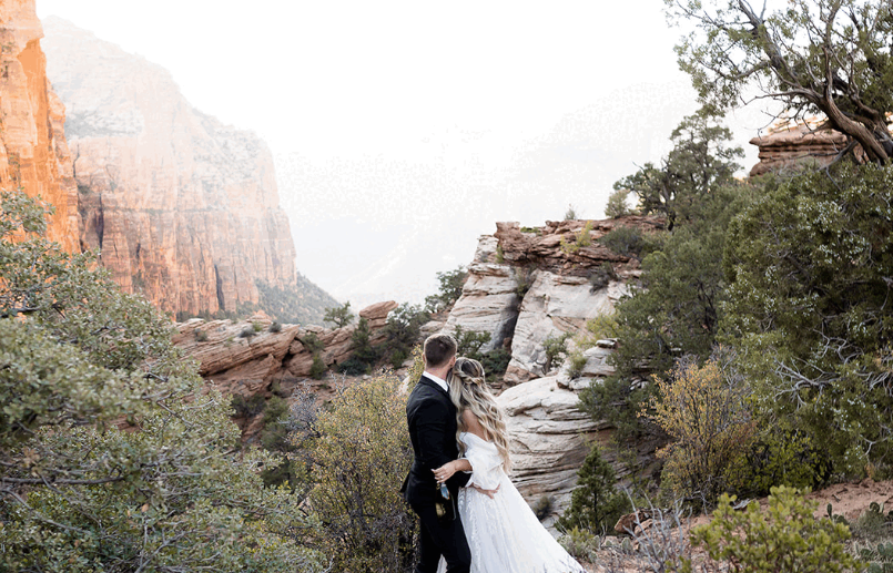 Couple standing together, gazing out at the towering red rock mountains of Zion National Park.