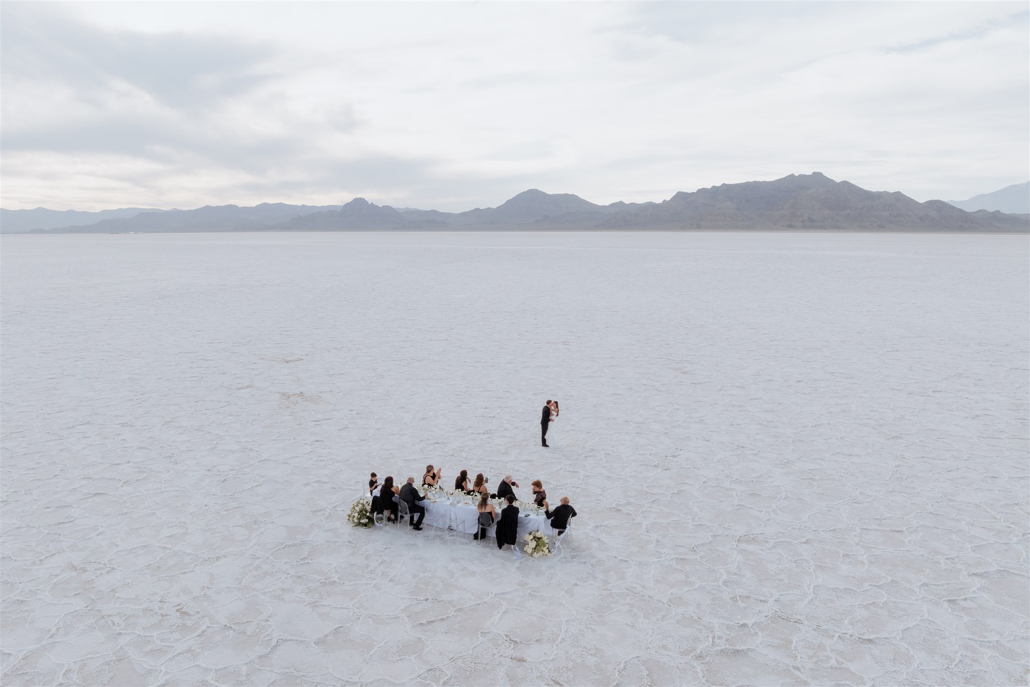 Aerial view of a green and white Bonneville Salt Flats wedding in Utah with bride and groom lying on the salt flats